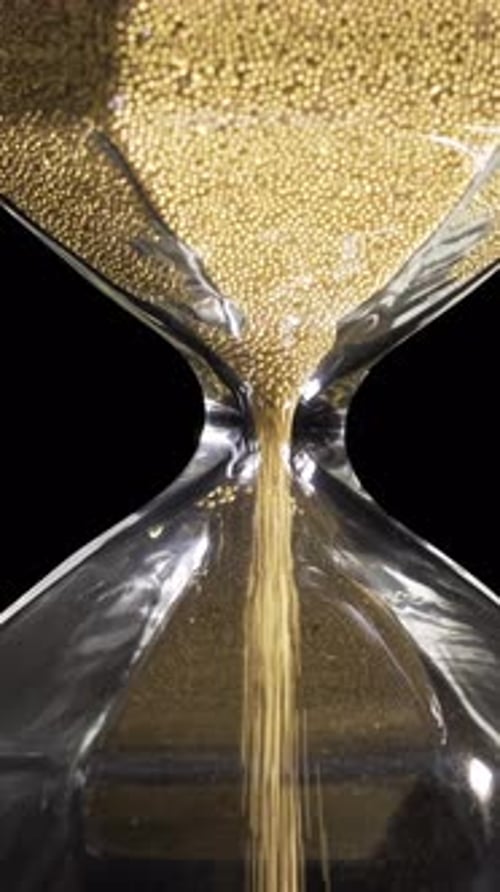 Golden Beads Fill Hourglass Against Dark Background