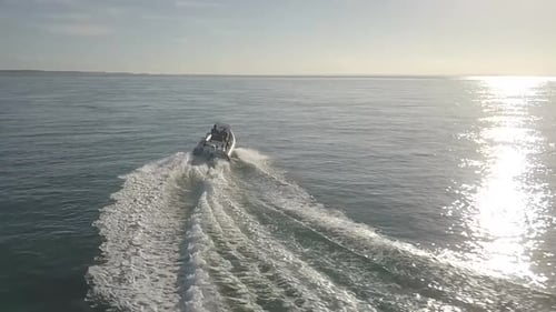 Slow motion aerial drone footage of motor boat travelling at high speed across smooth ocean water an