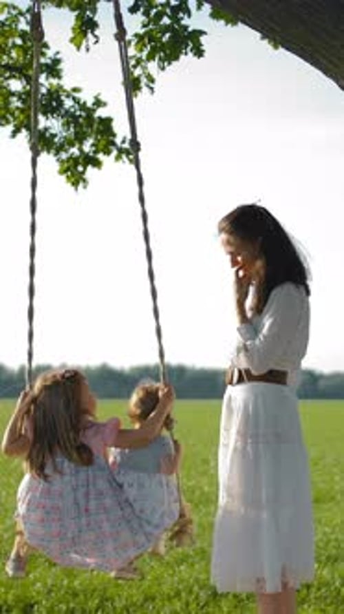 Two Girls on a Swing with Woman Nearby