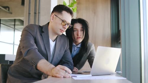 Two Business Professionals Have a Productive Discussion Over a Laptop in a Modern Office Sharing