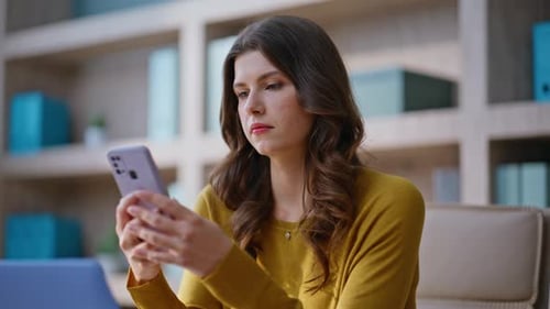 Empresaria decepcionada leyendo el mensaje del teléfono móvil sentada en el lugar de trabajo de cerca