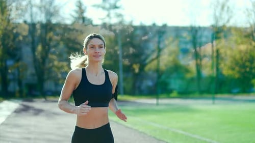 Adult athletic female runs on the track of an urban city stadium. A beautiful fit woman