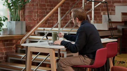 Konzentrierter männlicher Freelancer, der im grünen Coworking Space am Laptop arbeitet