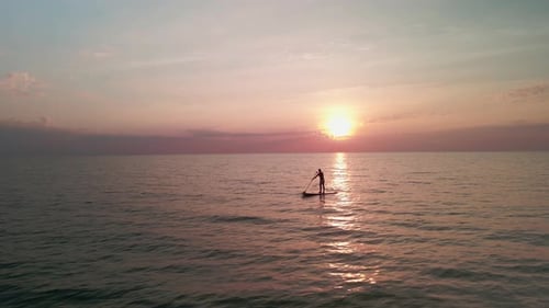 Drohnenaufnahme eines Mannes aus einem niedrigen Winkel beim Stehen Up Paddling, goldenes Sonnenlicht der Sonne, die im E untergeht