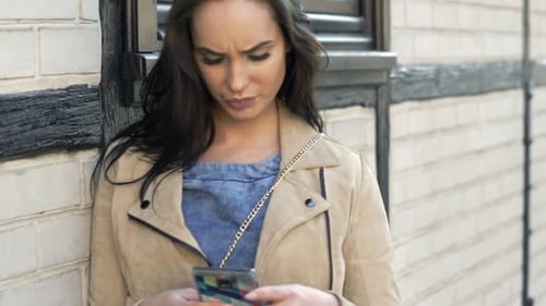Attractive brunette woman happily browsing internet on smartphone in the city