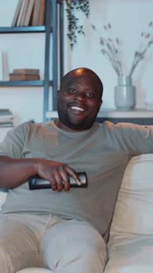 Smiling Man Sitting on Couch at Home Holding Remote