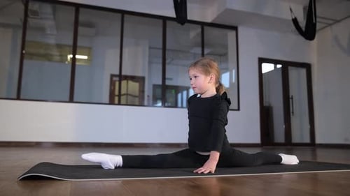 Child Girl Skillfully Performs Impressive Splits on a Yoga Mat in a Spacious Gym