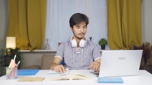 Young Man Studying at Desk with Laptop and Book