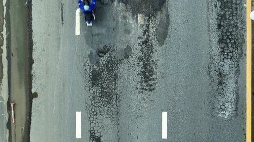Drone imagery shows an asphalt road in disrepair.