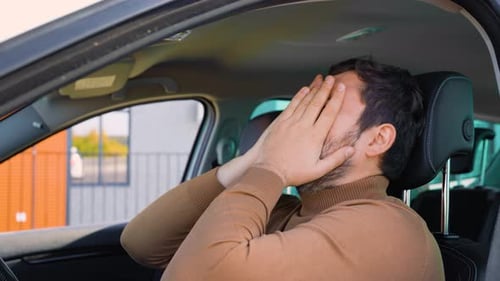 Man Rubs Face, Leans Back in Car Seat