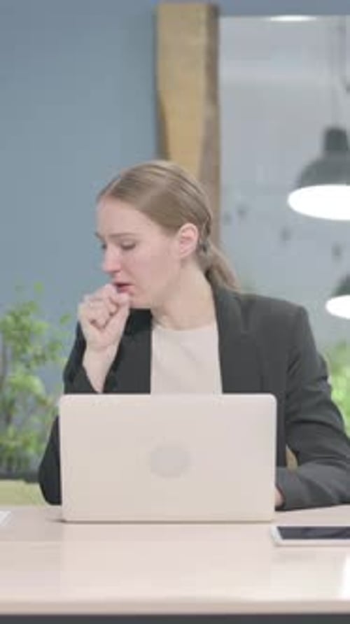 Woman Coughing While Working at a Laptop Indoors
