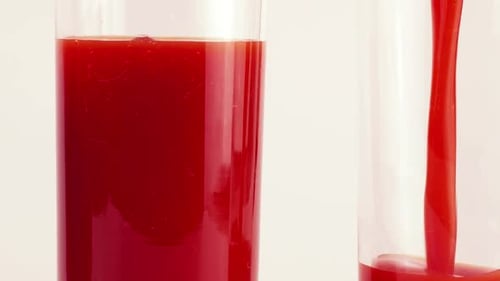 Tomato juice is poured into glass goblets. Slow motion.