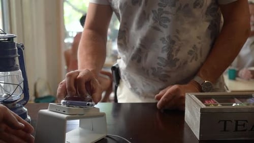 Ein älterer männlicher Kunde bezahlt die Rechnung über ein Smartphone mit kontaktloser NFC-Technologie in einem Café
