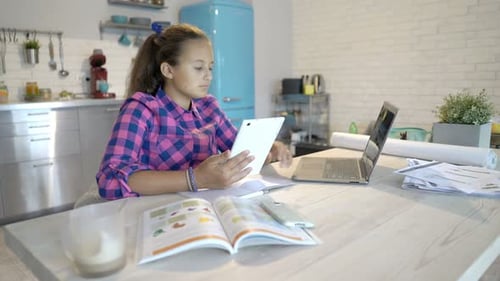 Teen Works on Tablet and Laptop in Kitchen