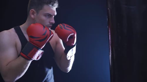 Male boxer. Strong athlete trains with focus and seriousness in dark gym.