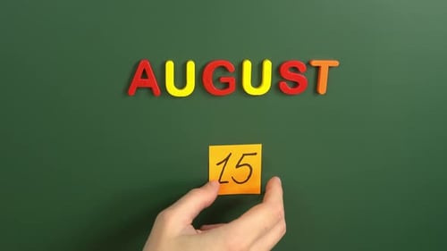 Hand sticking a sticker 15 August calendar day on school board. 15 date of august. Fifteenth day