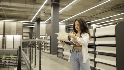Young Woman Looking Samples of Wallpaper at Catalogue in Household Store