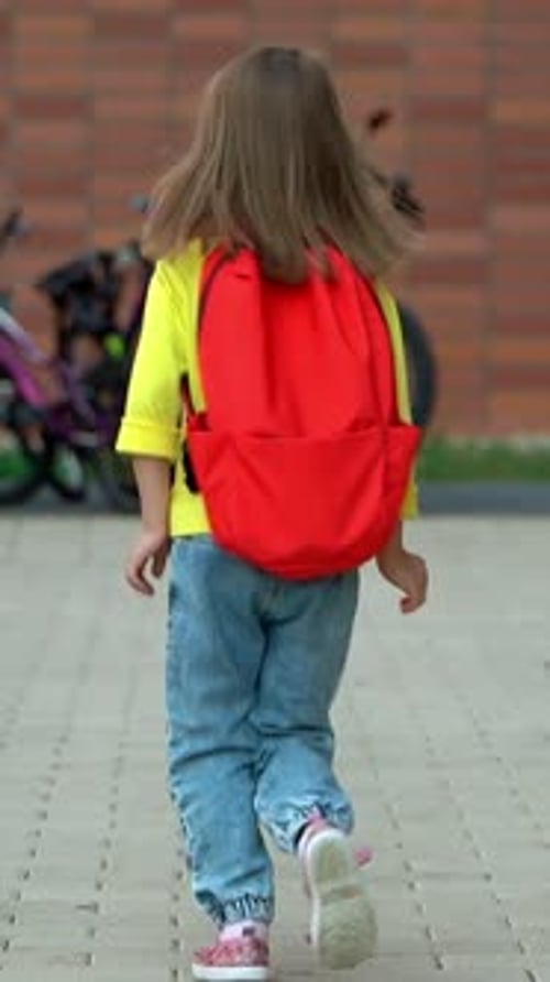 Rückansicht eines Mädchens, das mit Rucksack im Freien im Schulhof läuft