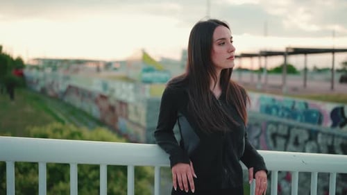 Pretty woman stands on bridge and looks away turns her head to the camera and smiles