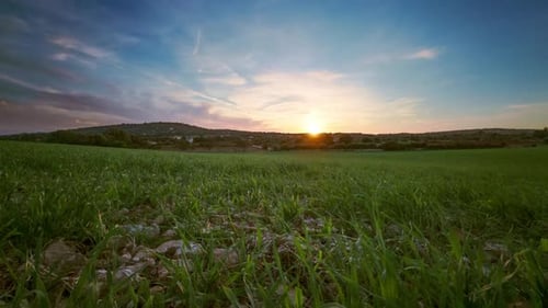 Stunning timelapse video of a green meadow, gentle hill, and floating clouds in a blue sky. Dramatic