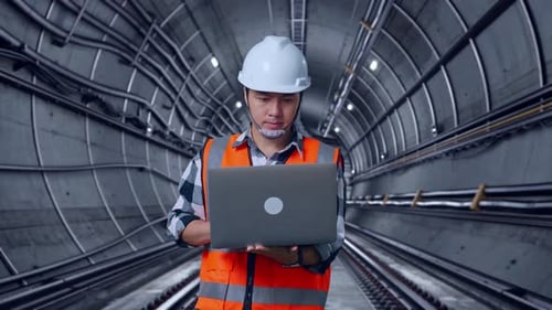 Asian Male Engineer Working On A Laptop In Subway Tunnel