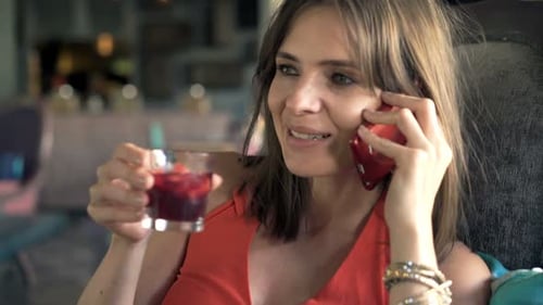 Young, Happy Woman Talking on Cellphone and Drinking Beverage Sitting in Cafe 30s