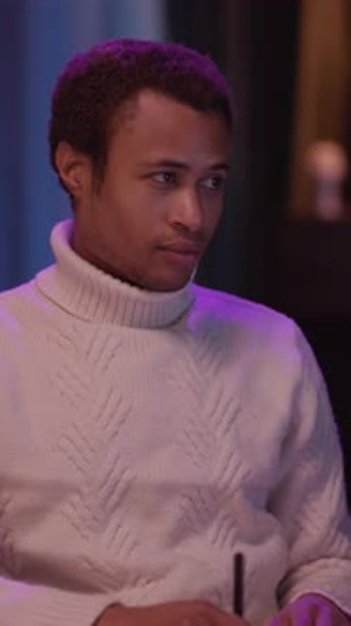 A Man in a Cozy Sweater Reflects at a Table Jotting Notes