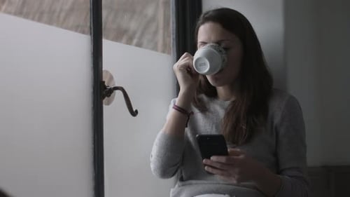 Woman Drinking Coffee and Using Smartphone Indoors