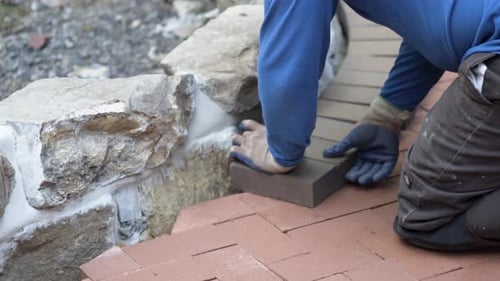 Closeup of putting brick pavers in place along an edge of a rock wall.