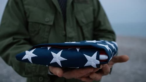 Man Holds Folded American Flag on Beach