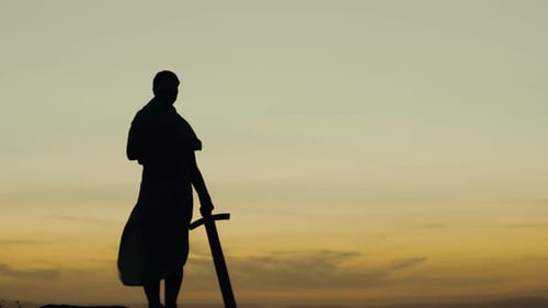 Silhouette Figure Raising a Sword at Sunset