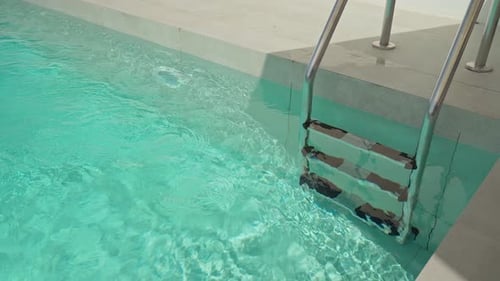 Sauberes Wasser plätschert sanft um die Stufen einer Metallleiter in einem türkisfarbenen Swimmingpool, der einladend ist