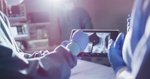 Video des Mittelteils zweier behandschuhter Chirurgen, die im Operationssaal über Röntgenaufnahmen auf einem Tablet diskutieren
