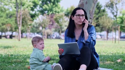 Young Mother with Tablet Computer Sitting with Little Son on Lawn Grass in Summer Park
