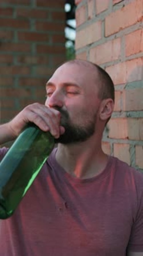 Un homme déprimé boit de l'alcool. Le concept de dépendance à l'alcool et de sans-abrisme. Vidéo verticale.