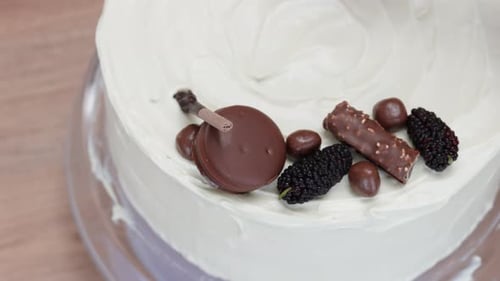 Top-down view of a pastry chef decorating a cake with circular chocolate cookies.