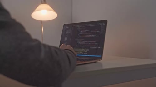De jeunes mains masculines apparaissent et se dirigent vers un ordinateur portable ouvert où le code d'édition du logiciel est activé