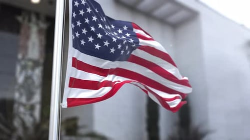 American Flag Waving on Flagpole Against Blurred Building