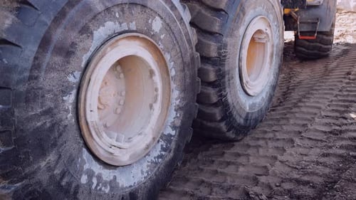 Close-up of large, muddy wheels on an industrial vehicle against a rugged terrain.