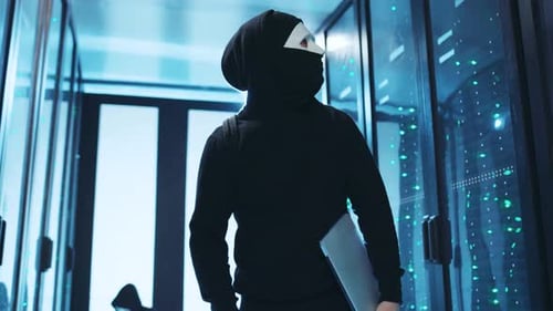 Masked Hacker with Laptop in Dark Server Room