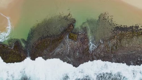Waves crashing on rocky shore in a tranquil coastal scene, aerial view