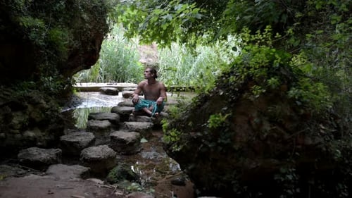 Homme caucasien assis sur des pierres au bord d'une petite rivière