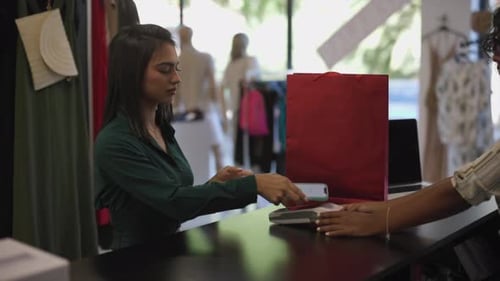 A woman completes a purchase in a clothing store by making a credit card payment using her smartphon