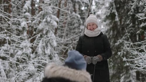 Happy Mother in Warm Clothes Rolls Son on Sled in Beautiful Snowy Forest