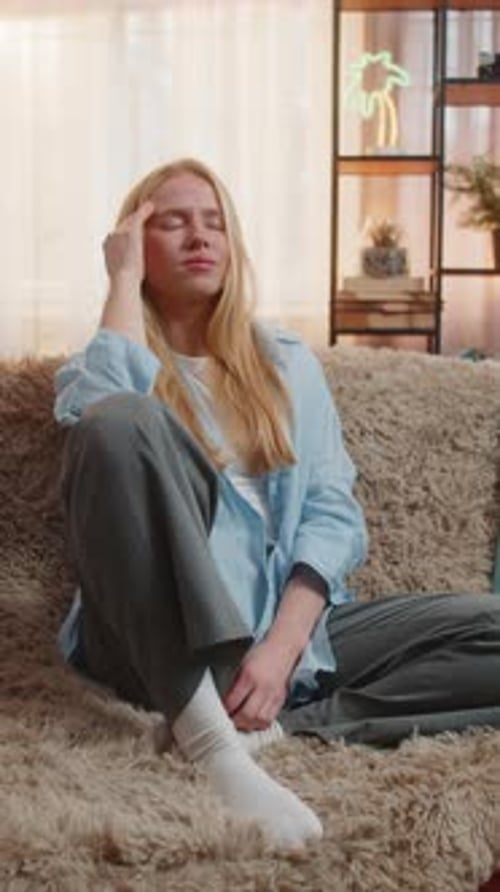 Young Woman Rubs Temples While Sitting Indoors