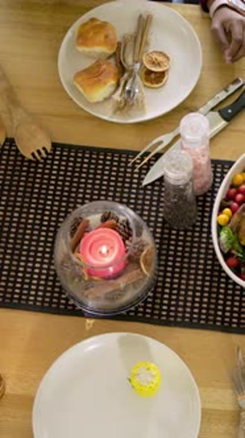Vidéo verticale : D'une main en haut à gauche, on place le rôti et le pain sur la table de la maison pendant que les invités s'installent