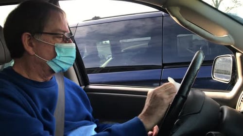 Man With Face Mask Wiping And Disinfecting Steering Wheel In The Car - handheld, close up