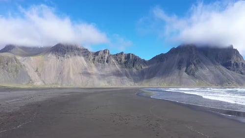 Aerial slow motion view of Vestrahorn mountains, Hofn and Atlantic ocean waves, Iceland