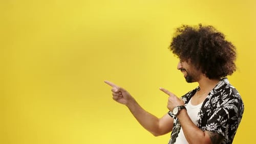 Young mixed race man points fingers with confidence in a yellow studio portrait