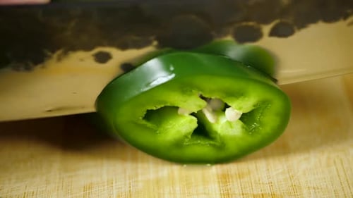 Chefkoch schneidet grüne Jalapeno-Pfeffer mit einem scharfen Messer von Hand auf das Schneidebrett zu einem Stapel